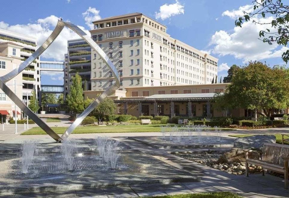 a large building with a fountain in front of it , surrounded by trees and grass at Juniper Hotel Cupertino, Curio Collection by Hilton