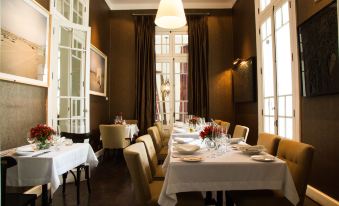 a long dining table with white tablecloths and chairs , set in a dimly lit room with large windows at Hotel B