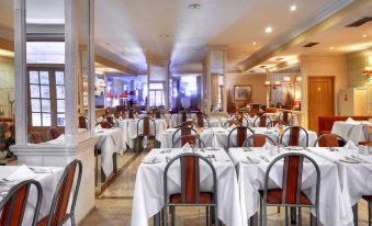 a large , empty restaurant with multiple tables set for diners , each table has a white tablecloth and has chairs at Hotel Kennedy Nova