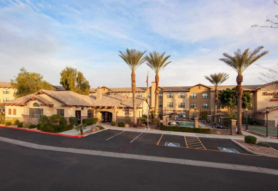 a large building with a parking lot in front of it , surrounded by palm trees at Residence Inn Phoenix Goodyear