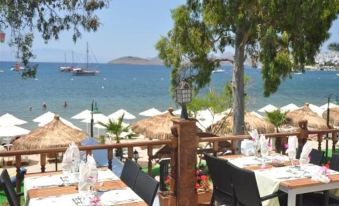 a beach restaurant with tables set up on the sand , umbrellas , and a view of the ocean at Manuela Boutique Hotel Bitez