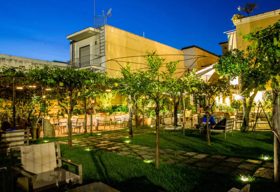 an outdoor dining area with several tables and chairs , surrounded by trees and lit up at night at Hotel Forum