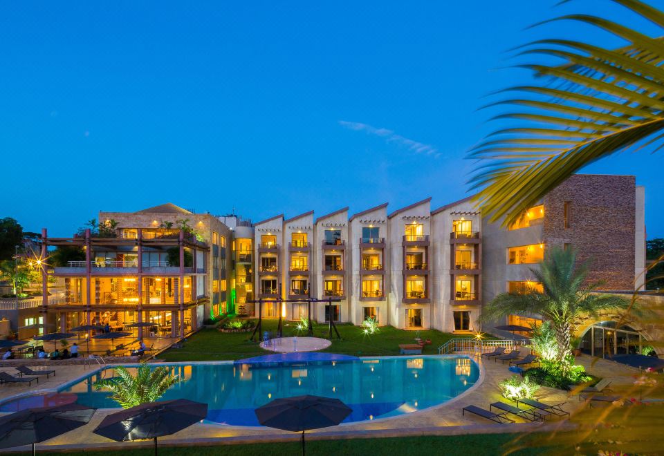 a large building with multiple floors and balconies is surrounded by a pool and palm trees at Peduase Valley Resort