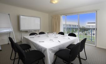a dining room with a table set for a meeting , featuring several chairs and a whiteboard at Quest Williamstown North