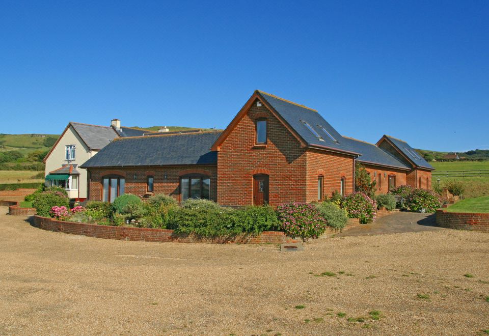 a brick house surrounded by a grassy field , with a fence surrounding the property and a dirt road leading up to it at Chale Bay Farm