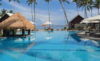 a large swimming pool surrounded by palm trees , with a view of the ocean in the background at Saletoga Sands Resort & Spa