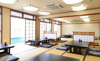 a japanese - style room with wooden walls , large windows , and multiple tables set for dining , under natural light from the ceiling at Hotel Hokke Club Kumamoto