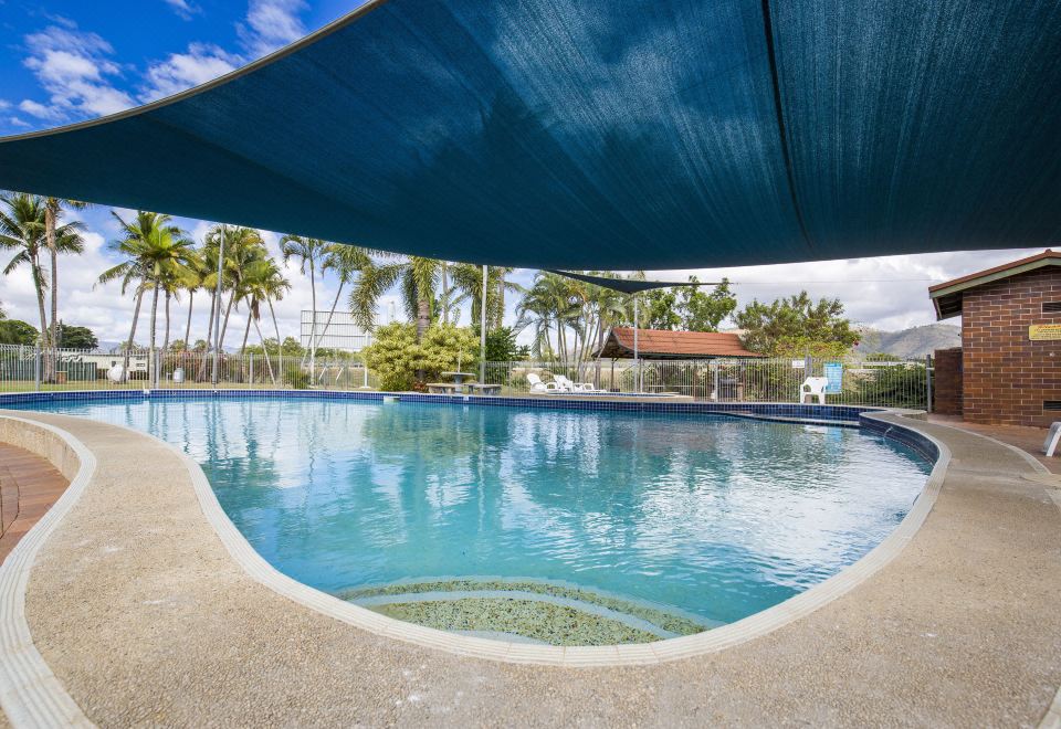 a large outdoor swimming pool surrounded by palm trees , with a blue tarp covering the area at Big4 Townsville Gateway Holiday Park