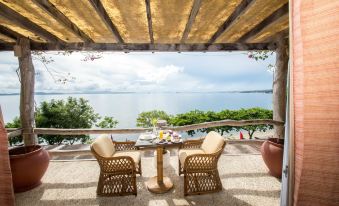 a patio with a table and two chairs overlooking a body of water , creating a serene and picturesque setting at Almont Beach Resort