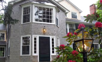 a gray house with a black door and windows , surrounded by greenery and red flowers at Harbourside Inn