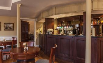 a dining room with a wooden dining table , chairs , and a bar area in the background at Leixlip Manor Hotel