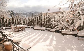 a snow - covered patio with a table and chairs , surrounded by trees and mountains in the background at Hotel Spa Azteca Barcelonnette