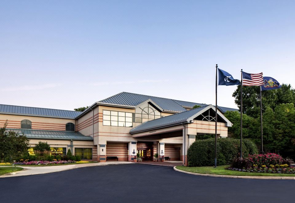 a large building with a flag flying in front of it , surrounded by trees and a parking lot at Desmond Hotel Malvern, a DoubleTree by Hilton