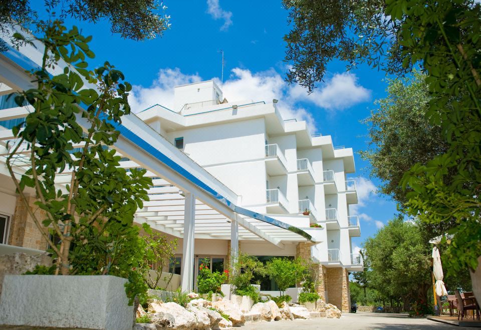 a large white building with a blue roof , situated on a street with trees and rocks at Hotel Orsa Maggiore