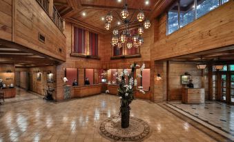 a large , well - lit hotel lobby with wooden walls , multiple chandeliers , and a reception desk , where guests are welcomed and at The Manor at Camp John Hay