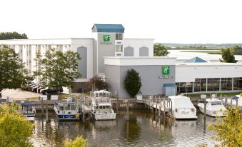 a marina with several boats docked , including a sailboat and a motorboat , located next to a hotel at Holiday Inn Grand Haven-Spring Lake