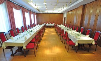 a long dining table with chairs and white tablecloths is set up in a large room at Hotel Alexandra