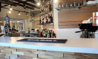 a bar with wooden countertops and a long black bar runner , as well as various bottles and cups on shelves at Rioshouse George-Inn