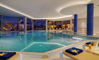 an indoor swimming pool with a blue water color scheme , surrounded by white walls and glass windows at Iberostar Selection Royal El Mansour