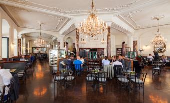 a large dining room with a chandelier , people sitting at tables in the center of the room , and a chandelier hanging from the ceiling at Hotel Central