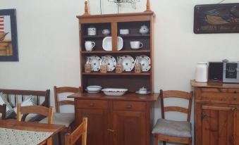 a wooden cabinet filled with a variety of dishes and utensils , surrounded by a dining table with chairs at MRS Simpson