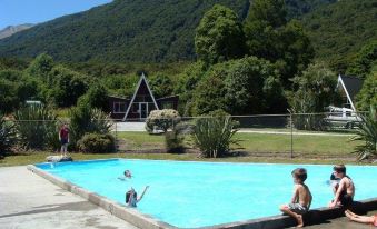 a young boy is sitting on the edge of a swimming pool , watching other people in the water at Wonderland Makarora Lodge
