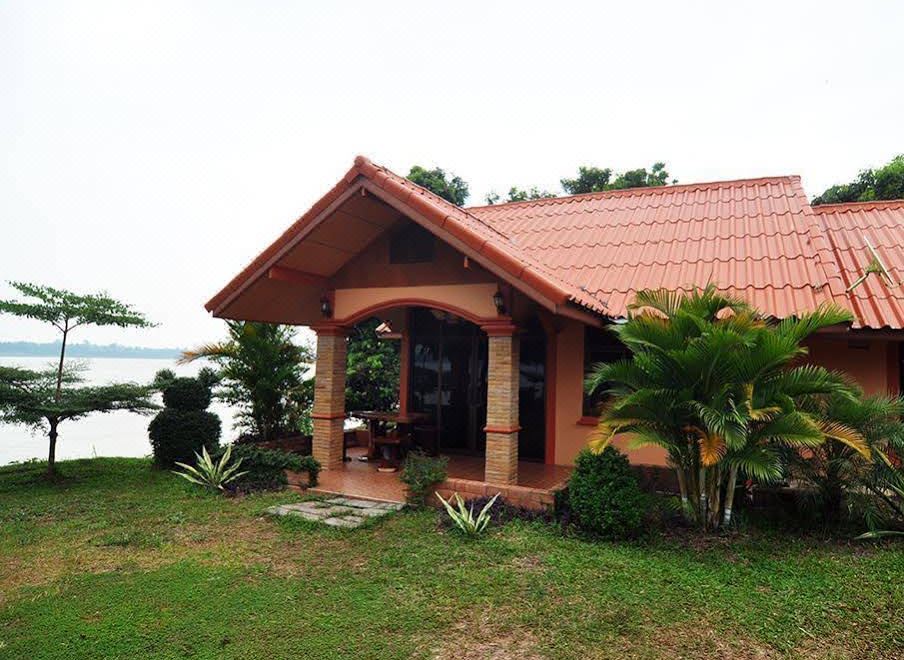a small wooden house surrounded by grass and trees , with a lake visible in the background at Baan Rim Khong Resort
