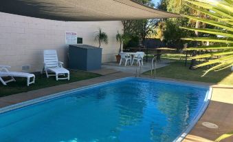 a backyard with a swimming pool , lounge chairs , and a dining table set up for a meal at Balonne River Motor Inn
