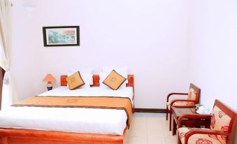 a neatly made bed with white sheets and orange pillows is in a room with chairs and a picture on the wall at Cay Thong Hotel