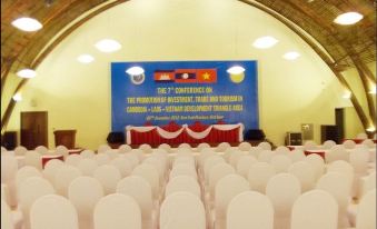 a large , empty conference room with white chairs and blue banners on the wall , under a large arch - shaped ceiling at Indochine Hotel