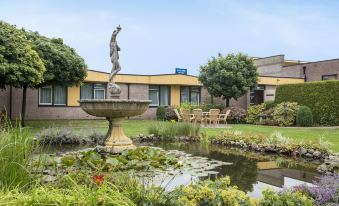 a courtyard with a fountain and a statue of a mermaid , surrounded by greenery and a building at Fletcher Hotel Steenwijk