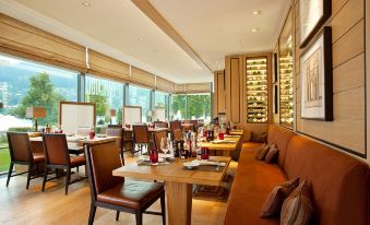 a restaurant with wooden tables and chairs , a long wooden bench , and large windows overlooking the city at Althoff Seehotel Überfahrt