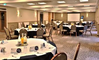 a large , well - lit conference room with round tables and chairs set up for a meeting or event at Manor House Hotel & Spa, Alsager