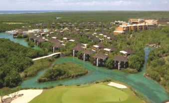 aerial view of a golf course with multiple buildings , trees , and a body of water in the background at Fairmont Mayakoba