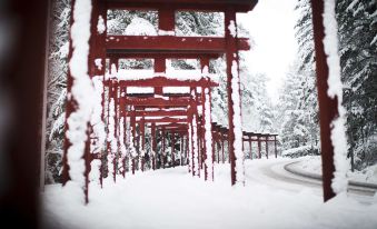 a red torii gate covered in snow , with a path leading up to it and trees surrounding the area at Yasuragi
