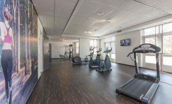 a well - lit fitness room with various exercise equipment , including treadmills and stationary bikes , as well as a large window that offers views of at Fletcher Kloosterhotel Willibrordhaeghe