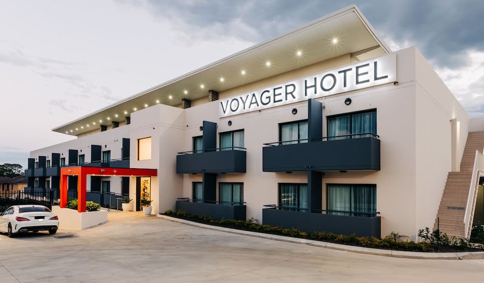 a large hotel building with multiple floors , a sign above the entrance , and balconies on both sides at Voyager Motel