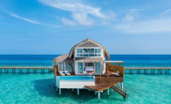 a tropical beach house with a wooden deck and clear blue water , under a sunny sky at JW Marriott Maldives Resort & Spa
