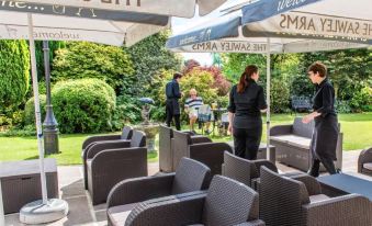 "a restaurant patio area with umbrellas , people , and tables , under a sign that says "" welcome to the cheese restaurant """ at The Sawley Arms