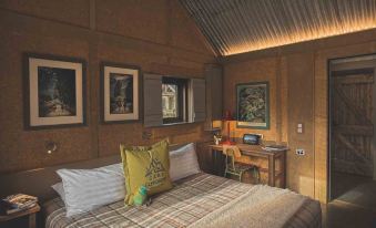 a cozy bedroom with wooden walls , a bed , and a desk , decorated with various artworks and objects at The Headwaters Eco Lodge