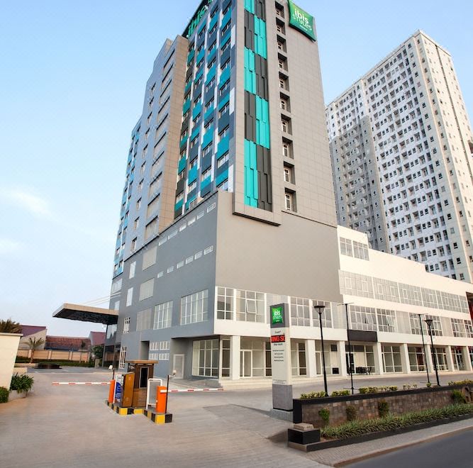 a tall building with multiple floors and a green sign on the top floor , surrounded by other buildings and a street at Ibis Styles Bekasi Jatibening