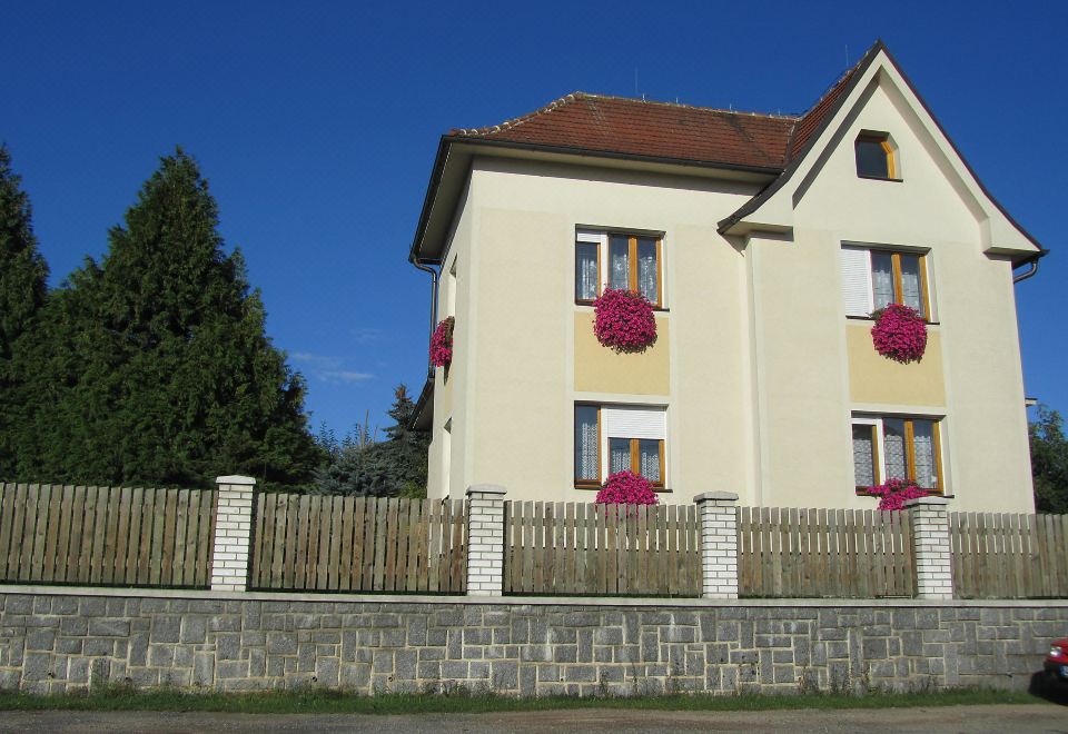 a two - story house with pink flowers hanging from the roof and a white fence in front of it at Nepomuk