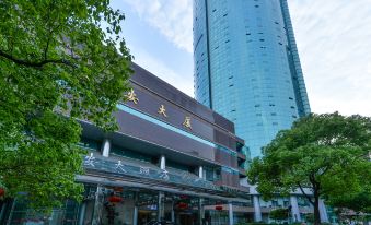 A large building with a hotel entrance in the front and a tall skyscraper behind it at Shanghai Baoan Hotel