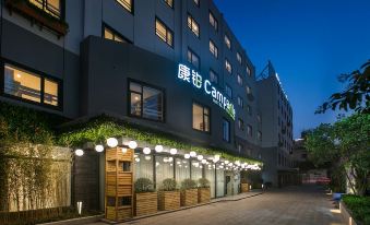 The entrance to a hotel is illuminated at night with a sign above it, surrounded by other buildings at Campanile Hotel (Shanghai Jing'an Temple)