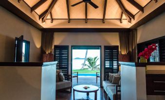 a living room with wooden furniture and a view of the ocean through a large window at Matamanoa Island Resort