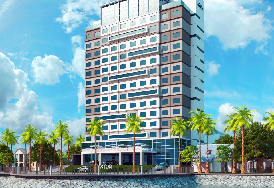 a tall , modern building with a red roof and many windows , situated near a body of water at Aston Kupang Hotel & Convention Center