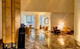 The lobby features chairs and tables in the middle, adjacent to an entryway that leads to the reception desk, providing a warm and inviting ambiance for hotel guests at Empire Hotel Hong Kong－Wan Chai
