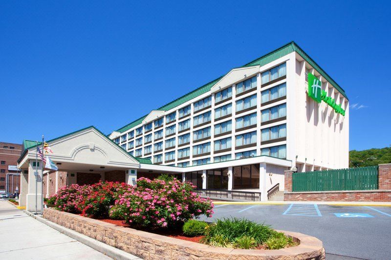 a large hotel with a green and white building , surrounded by bushes and flowers , under a clear blue sky at Ramada by Wyndham Cumberland Downtown