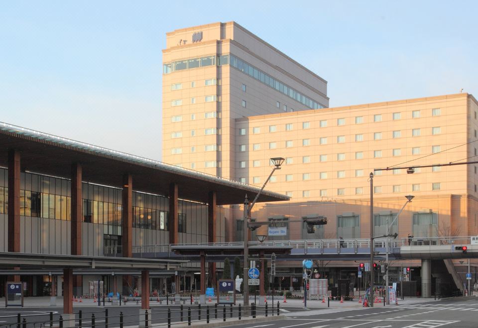 a city street with a tall building in the background and a bus stop in front of it at Hotel Metropolitan Nagano