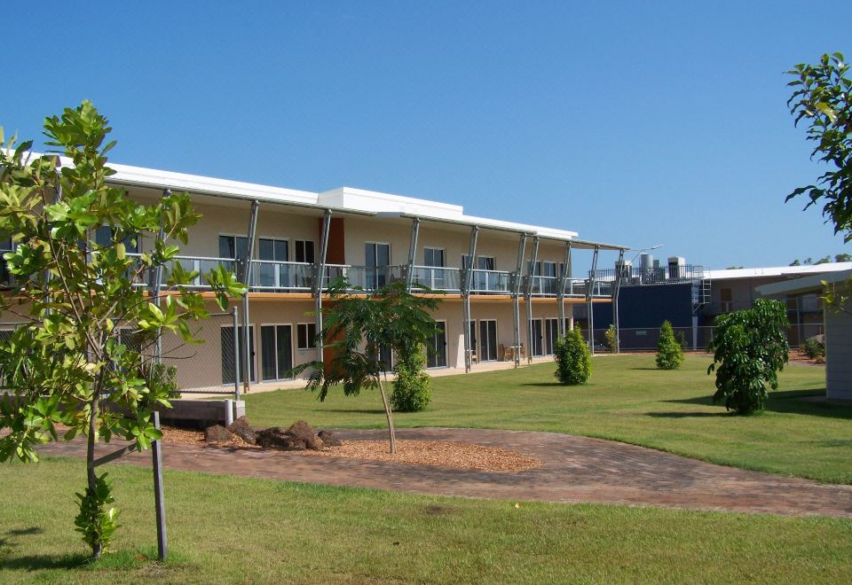 a large white building with multiple balconies and a green lawn in front of it at Club Tropical Resort Darwin